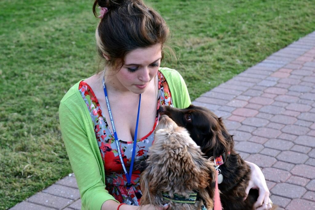 A young woman crouching on the grass, holding a spaniel against her cheek