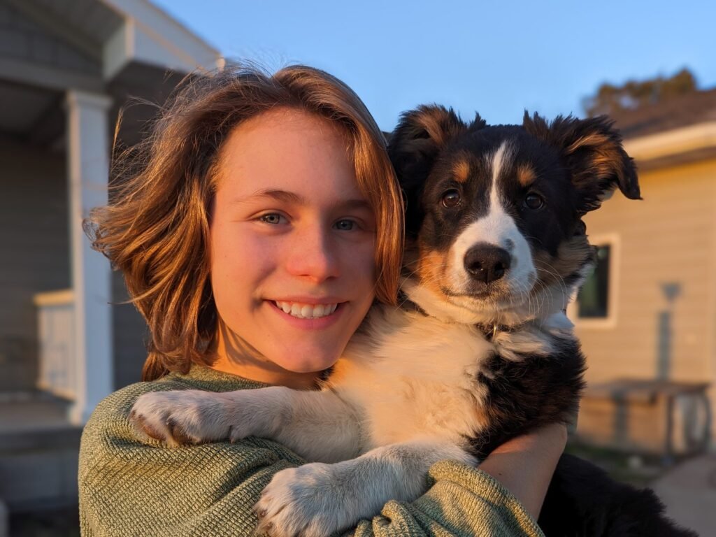 A woman holding a black and white puppy against her chest outdoors